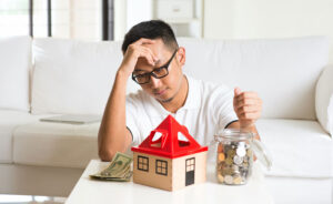 Stressed homeowner sitting with a model house and savings jar